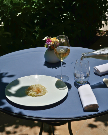 Table dressée en terrasse à La Table du Château avec mets gastronomique et verre de vin.
