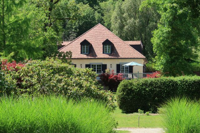 Vue d’une maison du domaine du Château de Germigney entourée d’un jardin verdoyant et d’arbres.